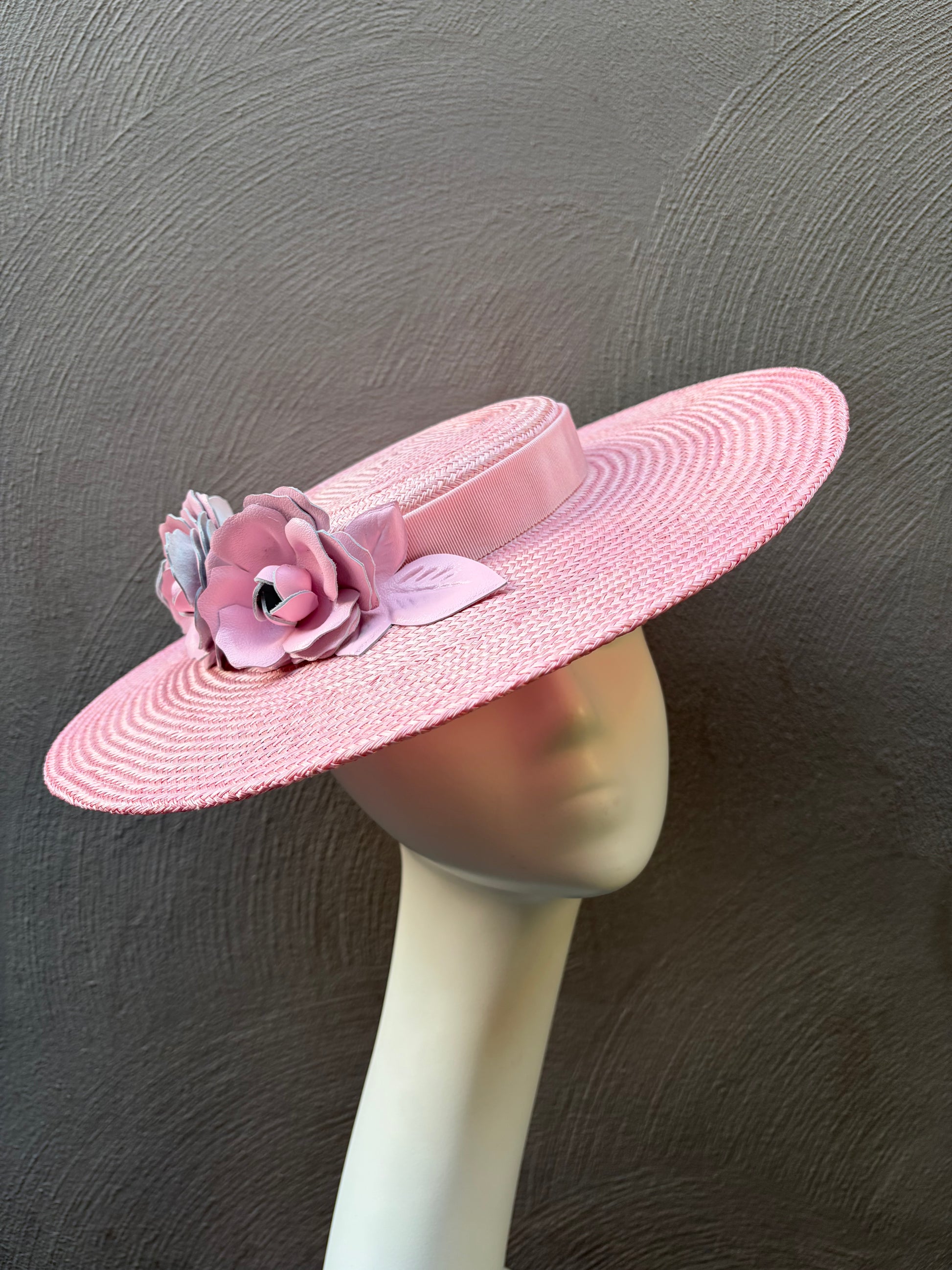 Hand‑dyed pink straw boater hat adorned with sculpted pink leather roses, wide brim, and adjustable fit.