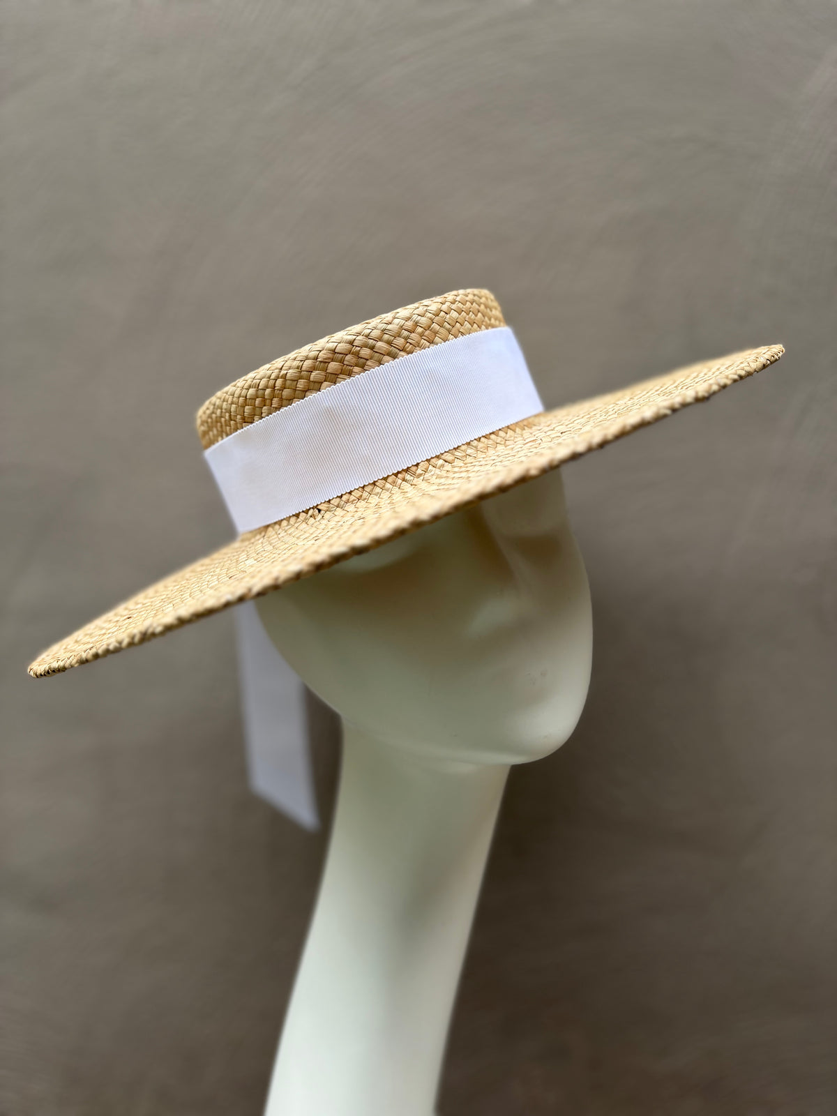 Elegant natural straw boater hat with a wide brim and classic flat crown, handcrafted for spring racing and special occasions.
