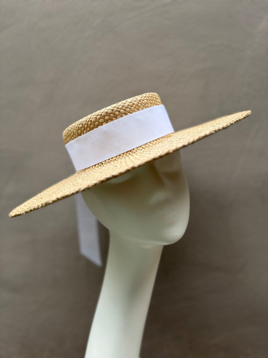 Elegant natural straw boater hat with a wide brim and classic flat crown, handcrafted for spring racing and special occasions.
