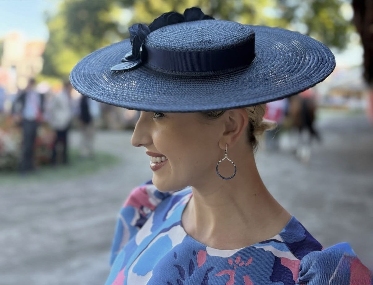 Navy wide‑brim boater hat with handcrafted leather roses worn by Acacia Clement at Saratoga Springs.
