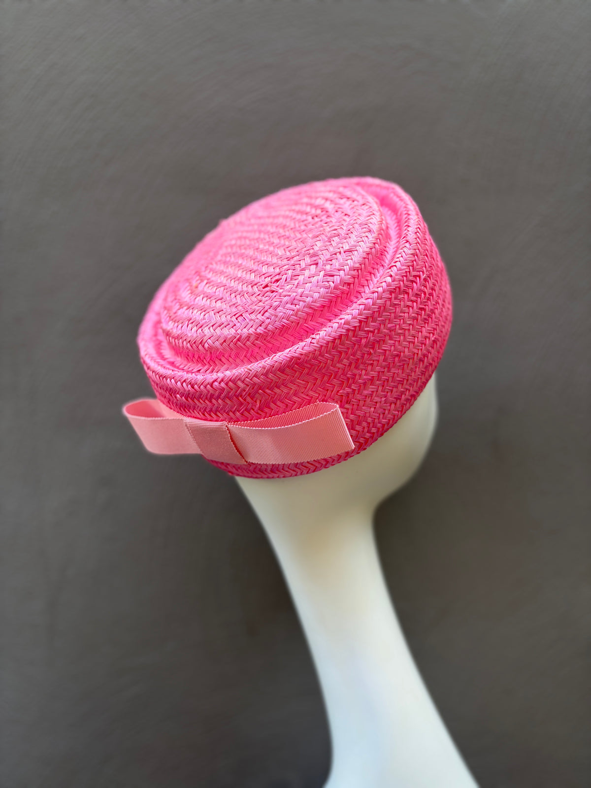 Couture pink straw pillbox hat with sculptural bow detail, designed for standout race day styling.